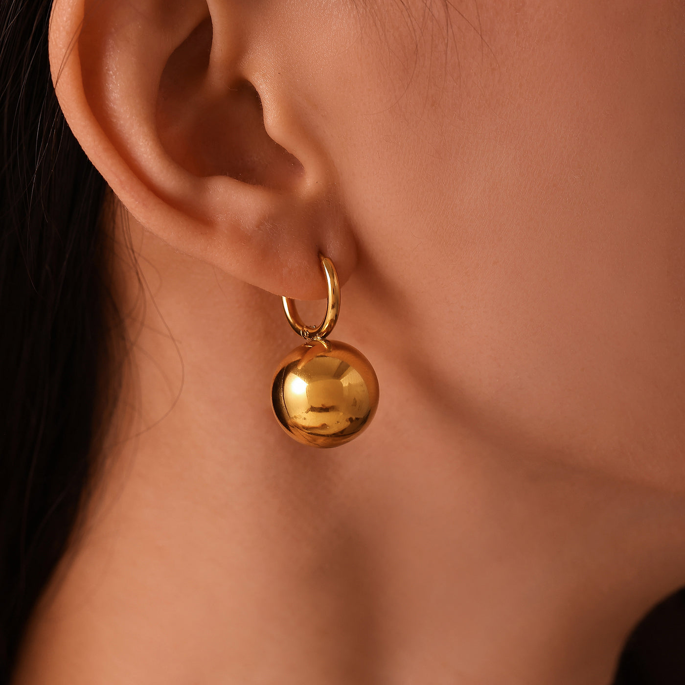 Model wearing a gold sphere drop earring with a gold-tone hoop