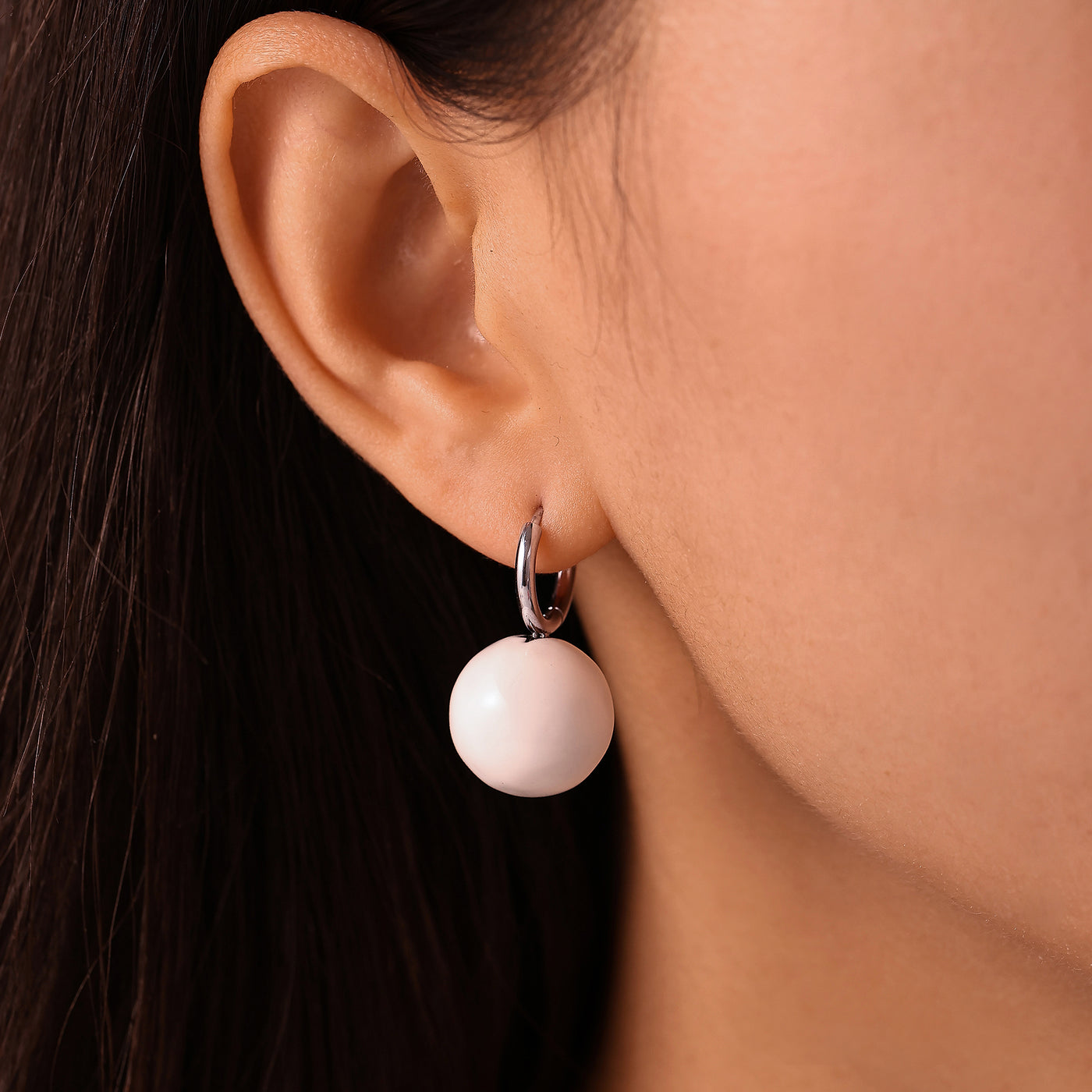 Side view of model wearing a white ball drop earring with a steel-tone hoop