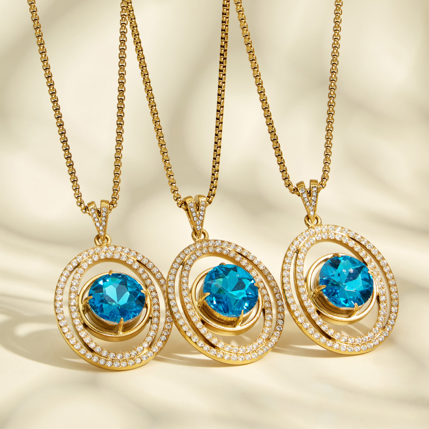 Three gold-tone necklaces with round blue glass halo pendants displayed side by side