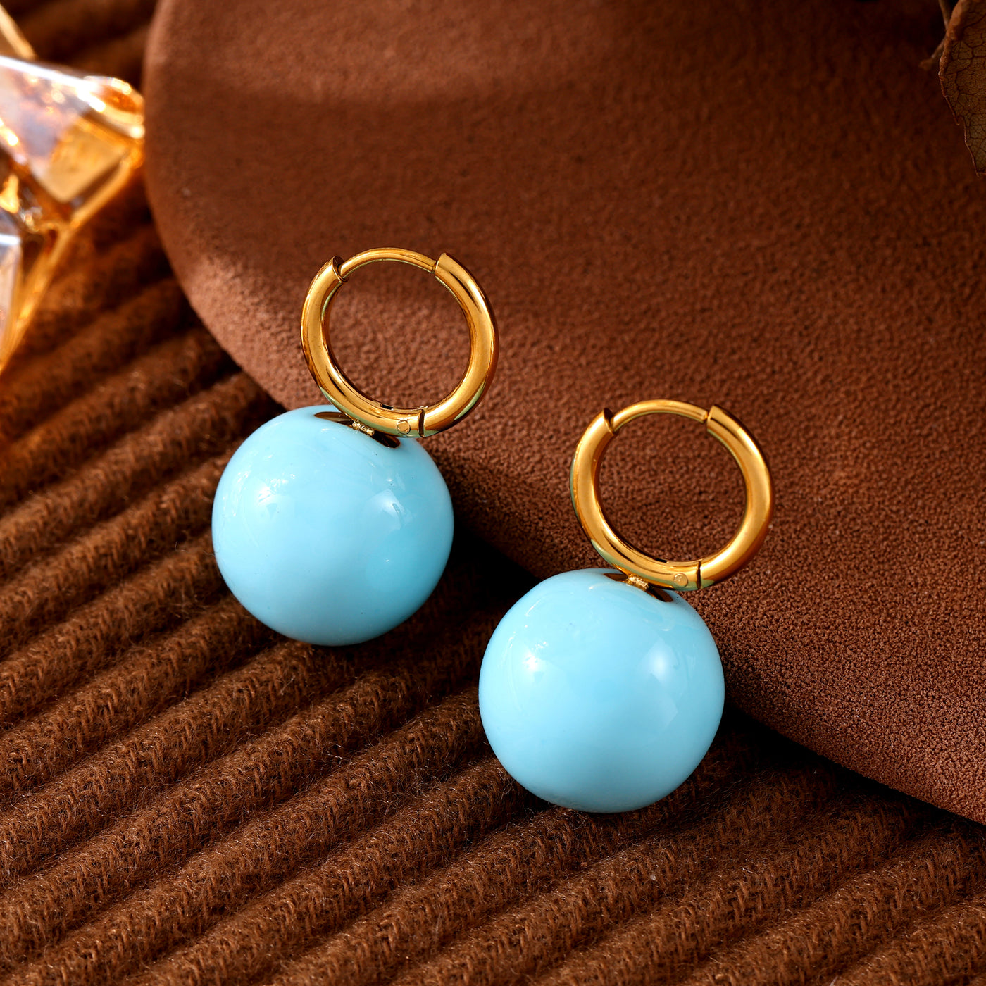 Close-up of light blue ball drop earrings with gold-tone hoops
