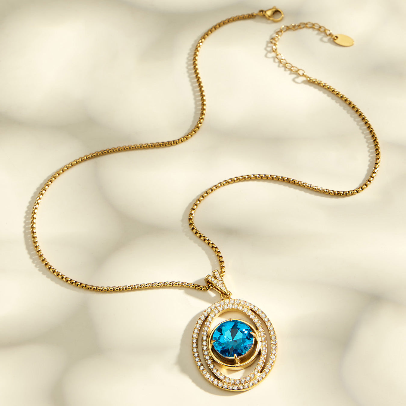 Gold-tone blue glass pendant necklace laid in a soft curve on a cream background