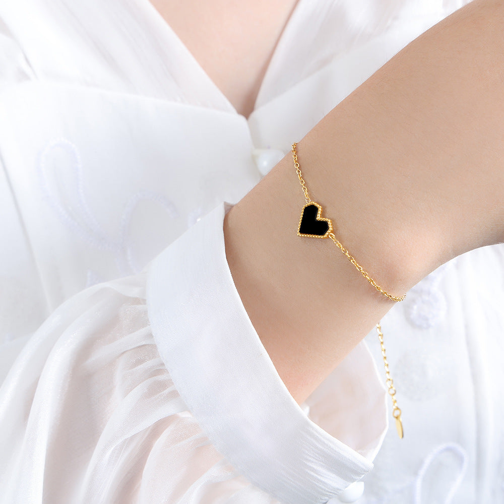 Minimalist black heart charm bracelet in gold stainless steel shown on a model's arm.