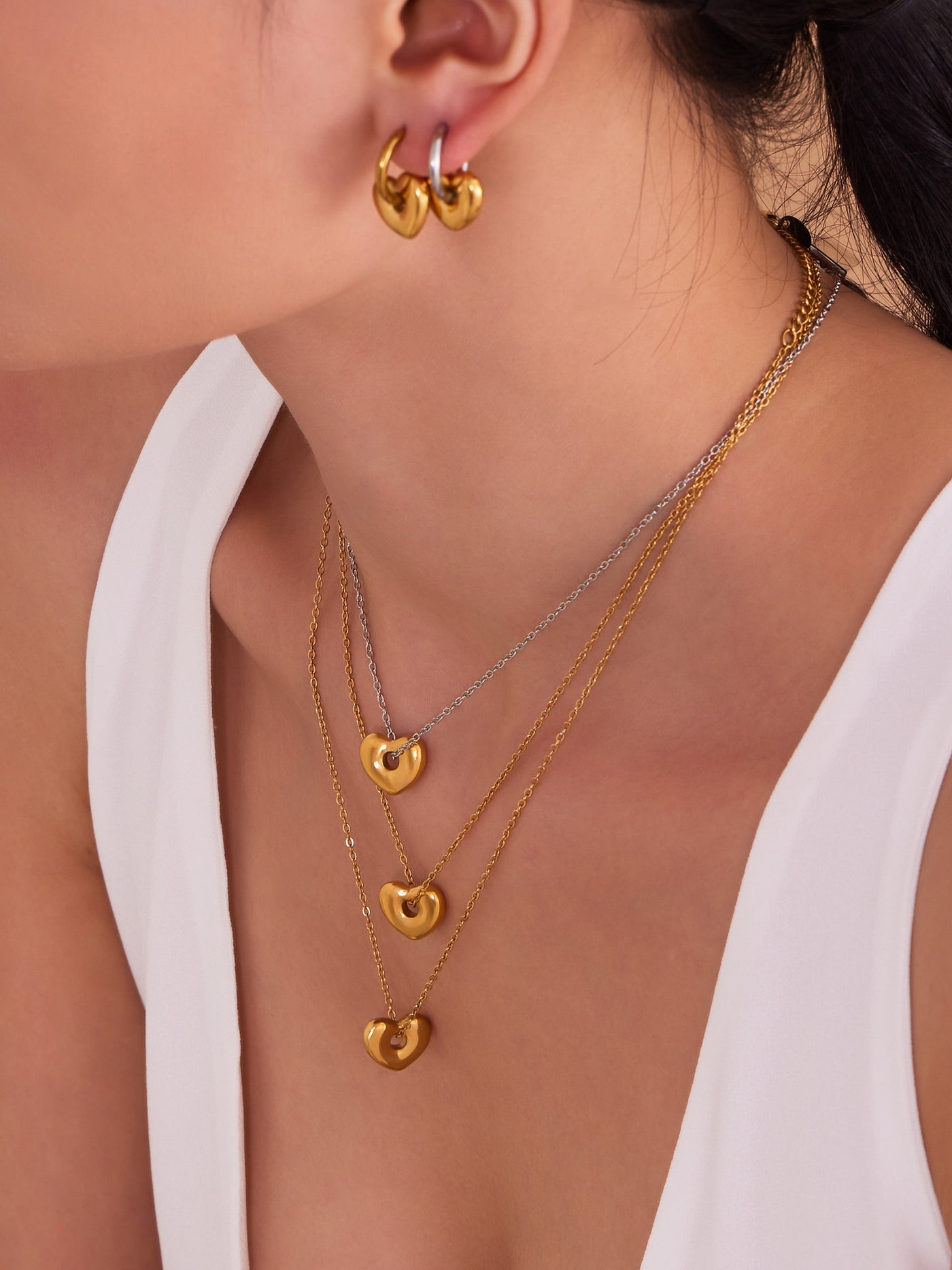 A woman wearing three layered 18K gold plated puffed heart necklaces made of hypoallergenic stainless steel.