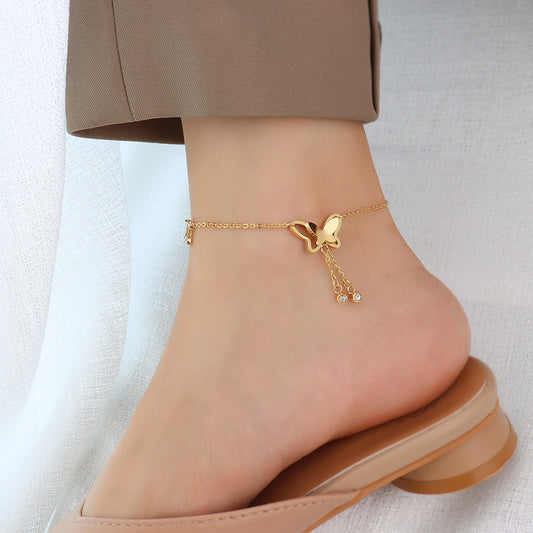 Close-up of dainty gold butterfly tassel anklet worn on woman's foot, delicate chain and playful tassel detail for beach styling