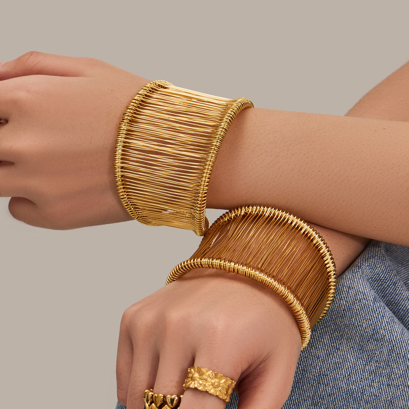 Two wide wire cuff bracelets in gold PVD plated 316L stainless steel worn on both wrists, modern statement fashion jewelry