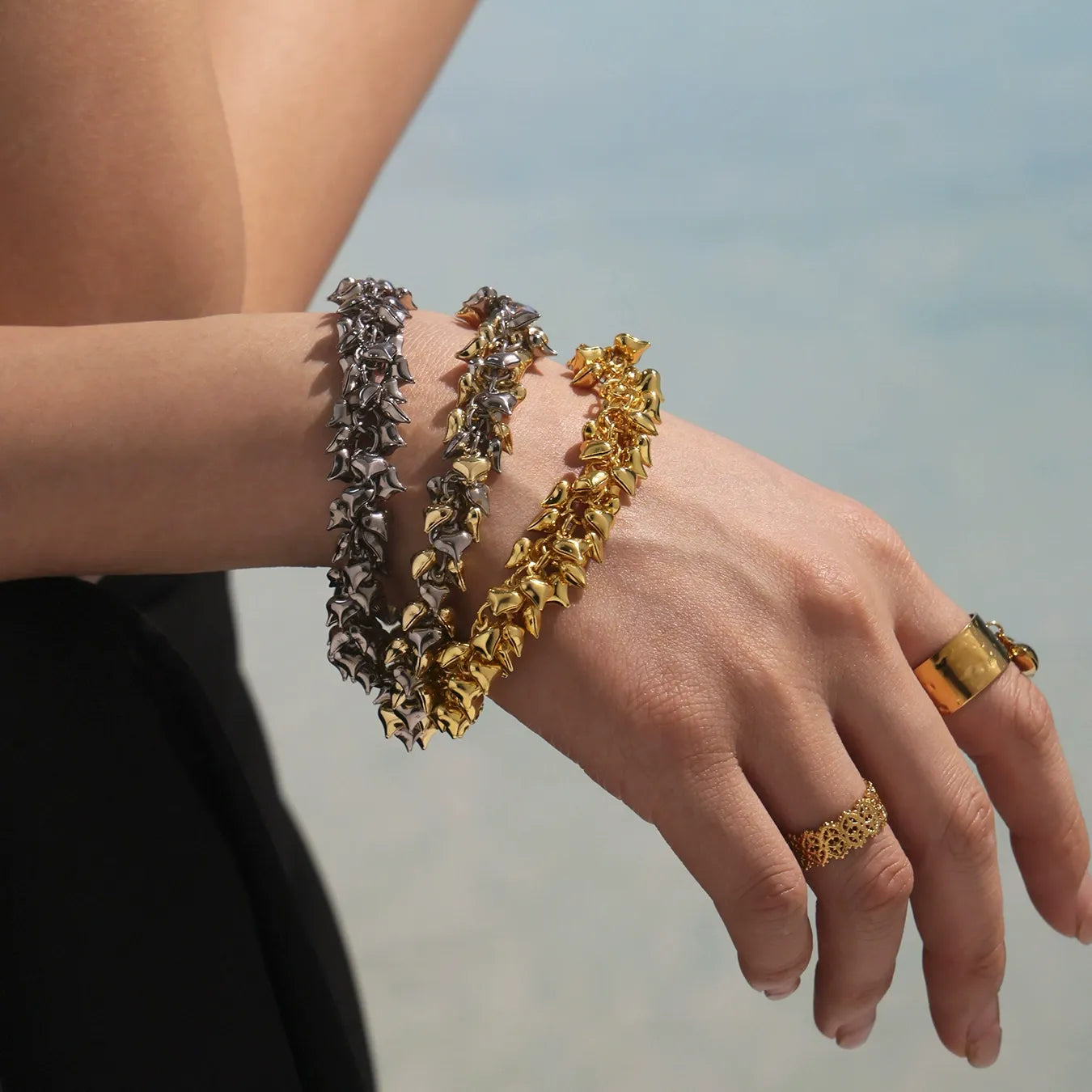 Two-tone 316L stainless steel heart charm bracelet held by model near beach background