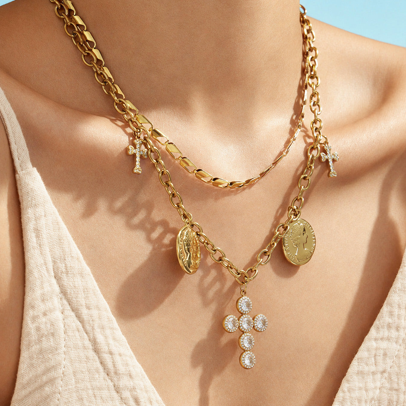 Close-up of a model wearing a clear zircon cross necklace layered with gold-tone coin chains