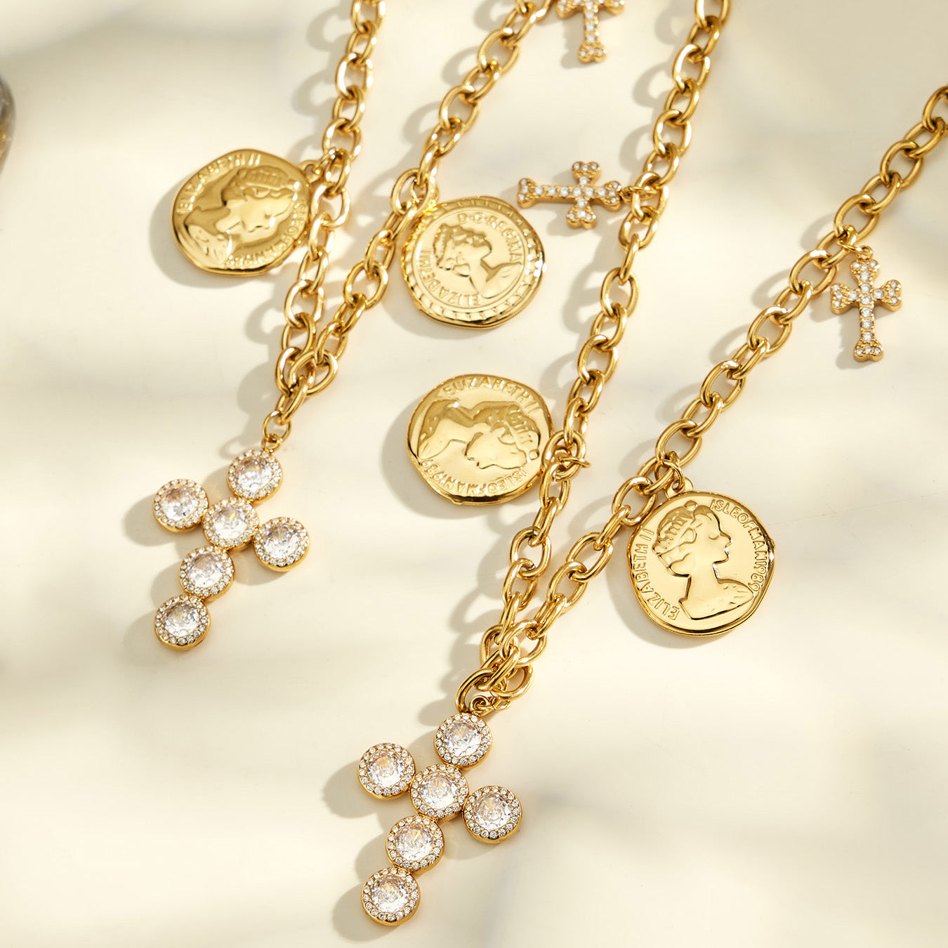 Gold-tone layered chains with coin pendants and cross charms arranged in a detailed flat lay