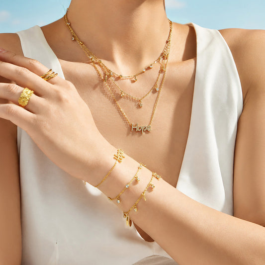 Model wearing gold celestial charm necklace and bracelet with star, moon, lightning and HOPE designs