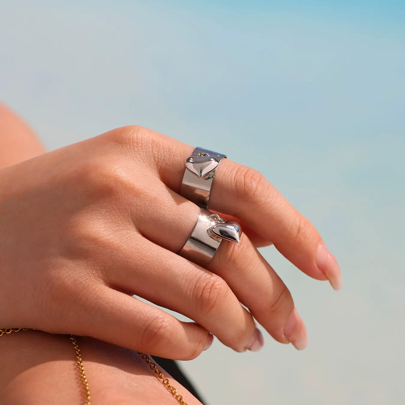 A woman wearing the chunky gold hypoallergenic wide band ring with a dangling heart charm on her hand.