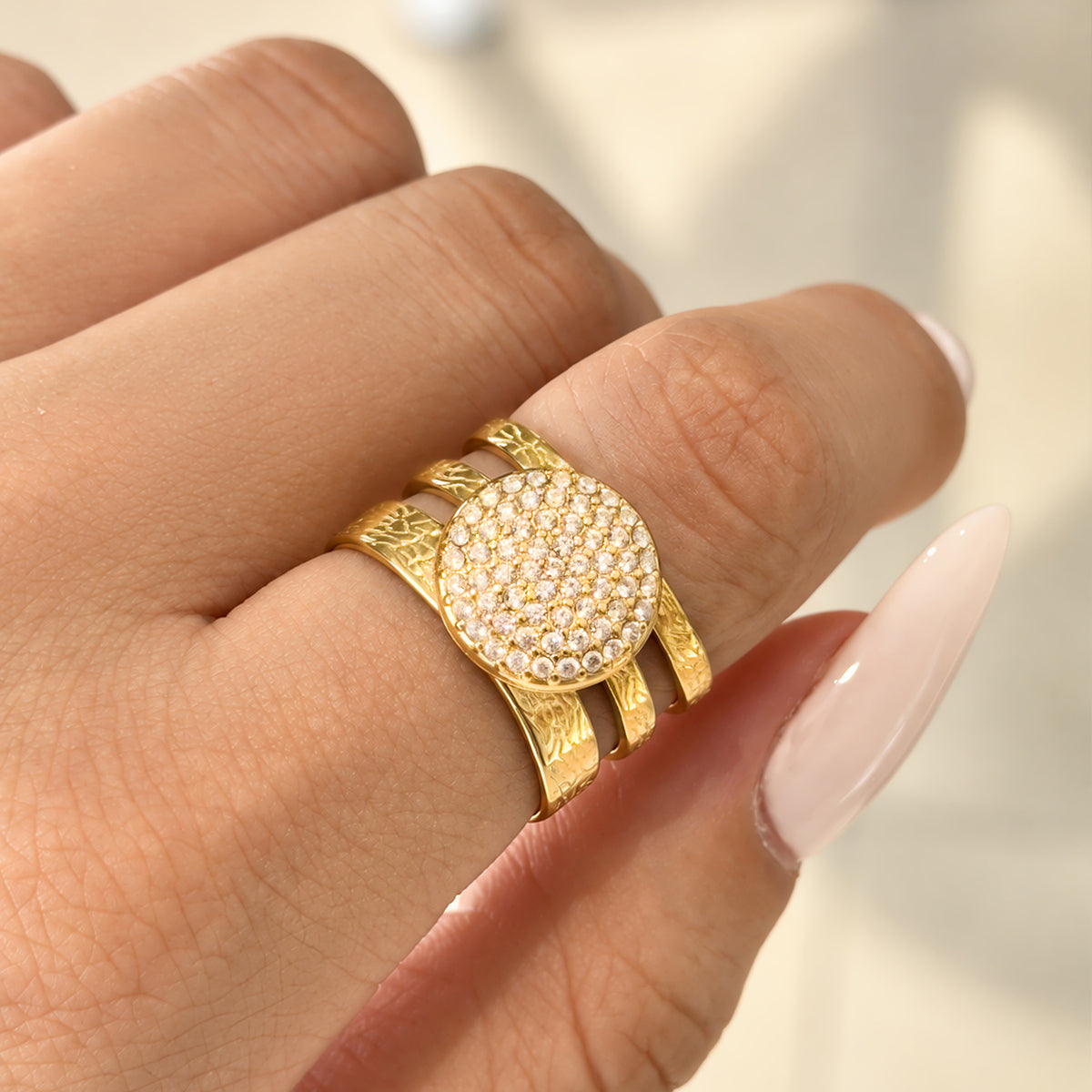 A421 gold-tone stainless steel ring worn on a finger, featuring a round face covered with clear stone accents