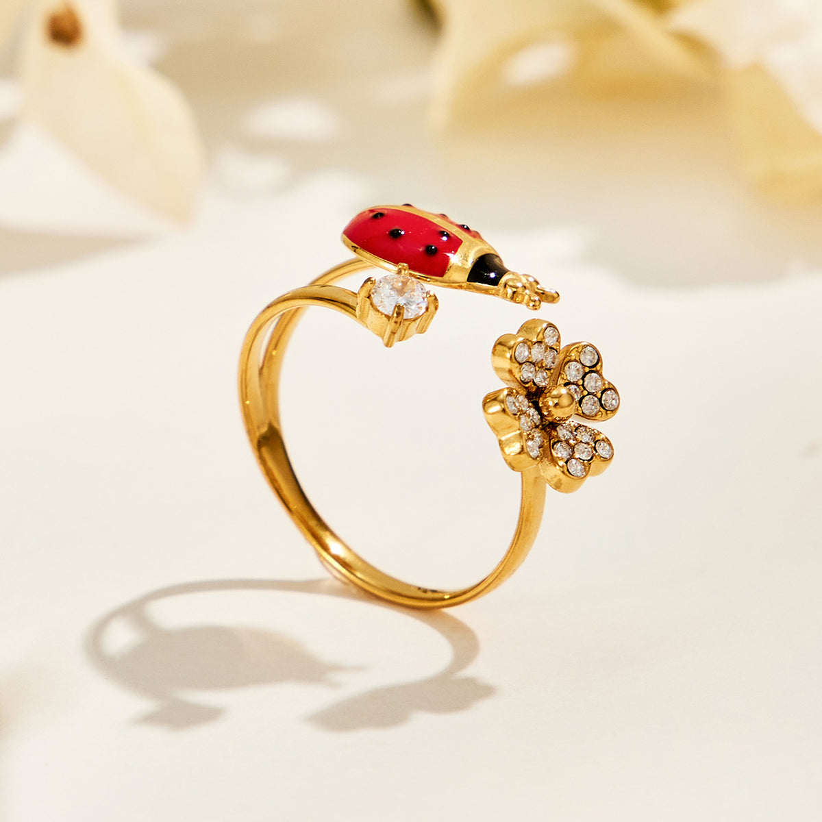 A445 gold-tone stainless steel ladybug and flower open ring standing on a cream surface with soft shadows