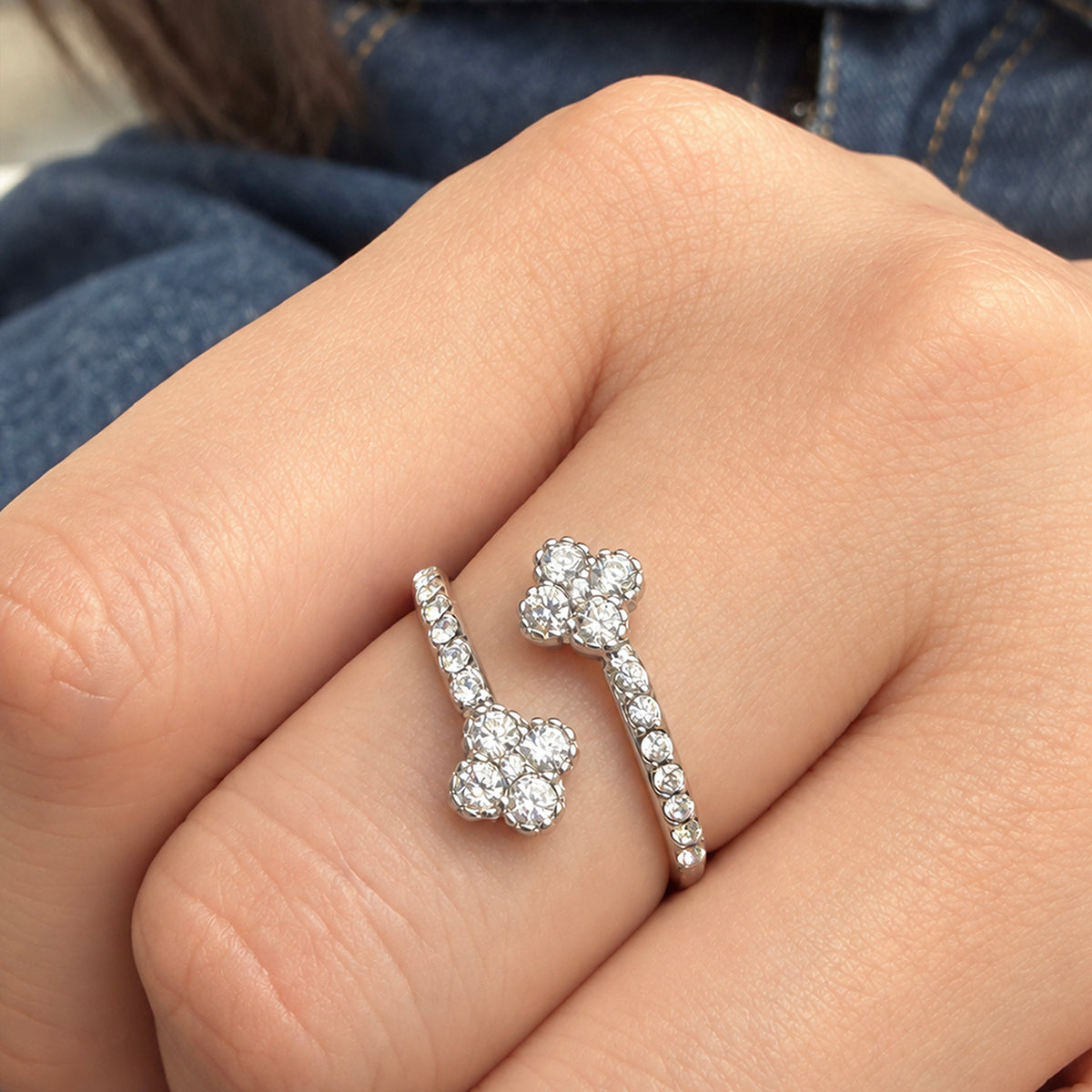 A446 steel-tone stainless steel open ring worn on a finger, showing two four-petal flowers and clear stone accents