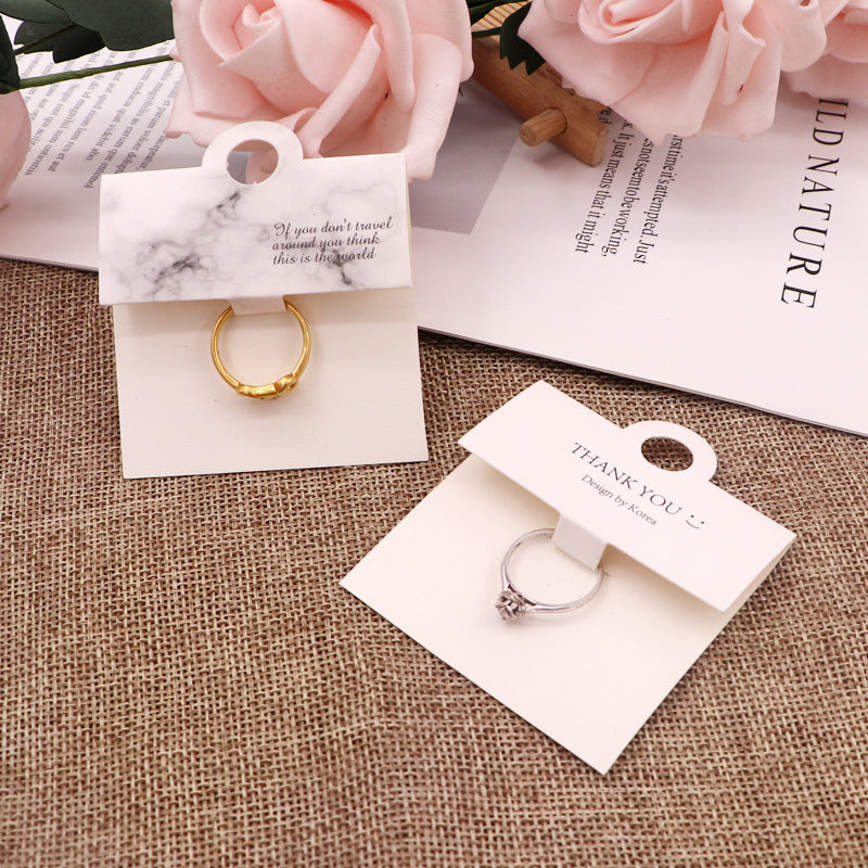 Black and white ring display cards arranged with jewelry on a neutral fabric background