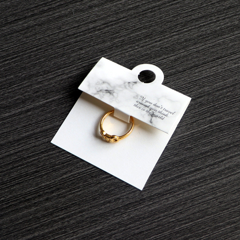 White marble-style ring card displaying a gold-tone ring on a dark surface