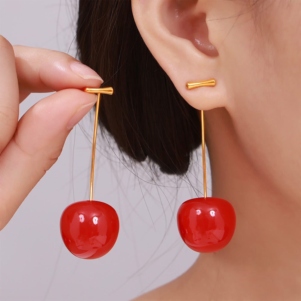 Model holding a pair of bright red cherry drop earrings beside her face