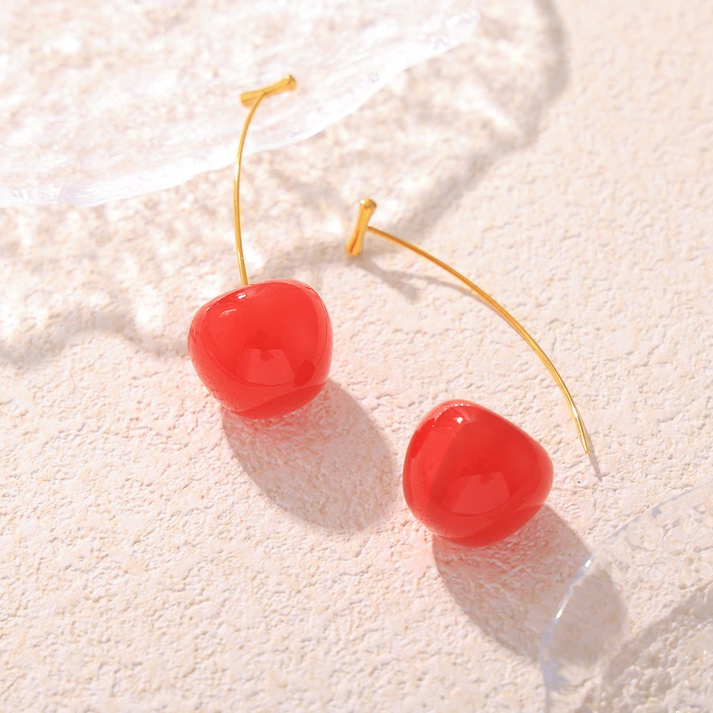 Bright red resin cherry earrings with slender gold-tone stems in a flat lay