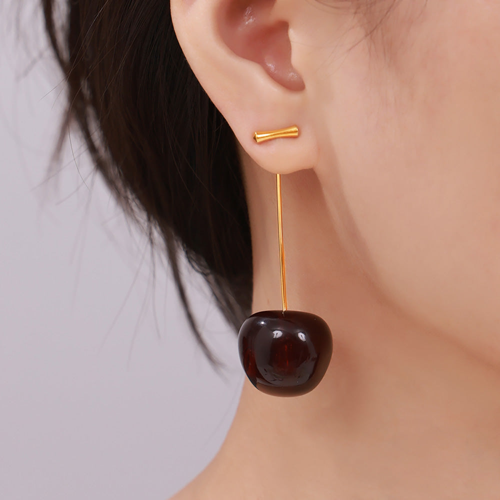 Close-up of burgundy cherry drop earrings worn with a neutral outfit