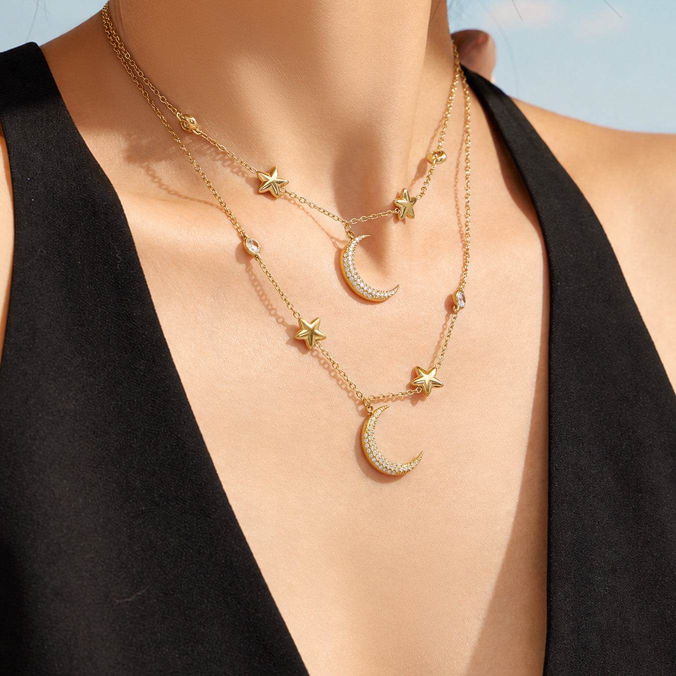 Model wearing a layered celestial star and moon necklace with a black outfit