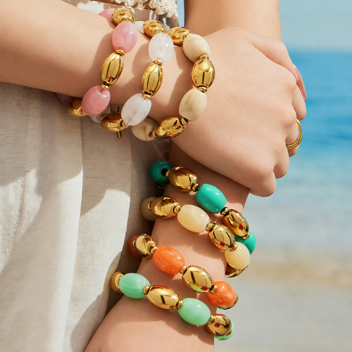 Model wearing stacked pink, white, ivory, yellow, green and orange resin bead bracelets with gold-tone accents