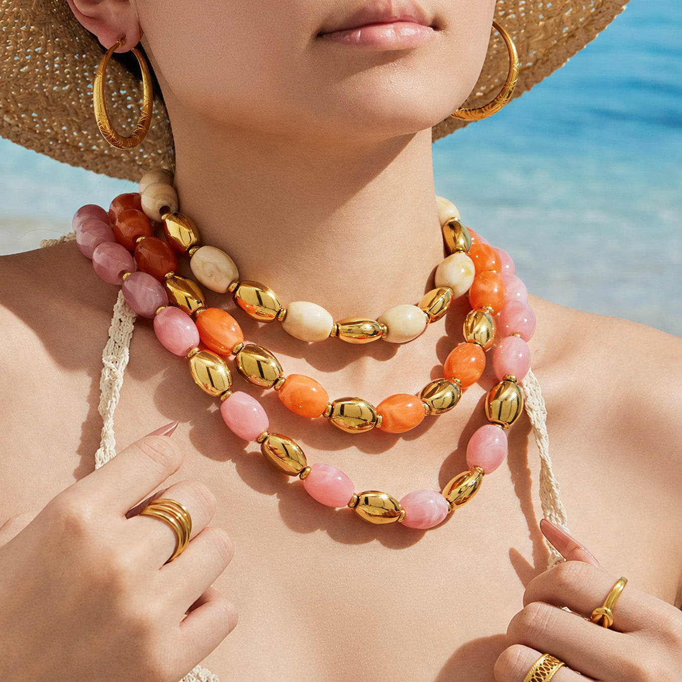 Model wearing layered pink, ivory and orange resin bead necklaces with polished gold-tone accents