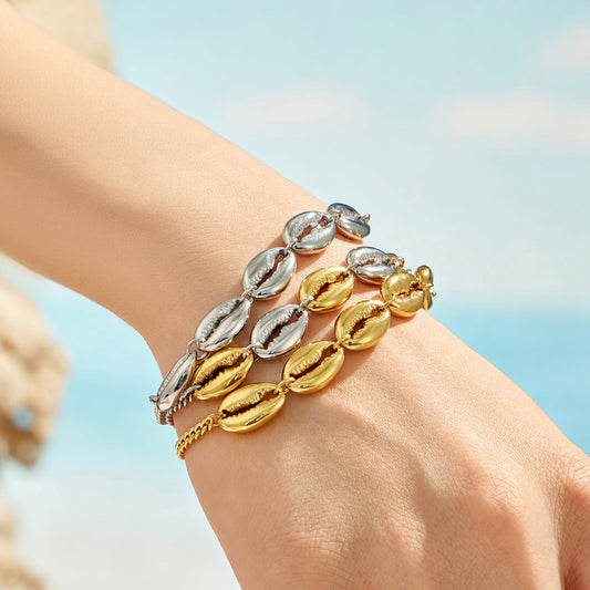 Model wearing layered cowrie shell link bracelets in steel, gold and two-tone finishes