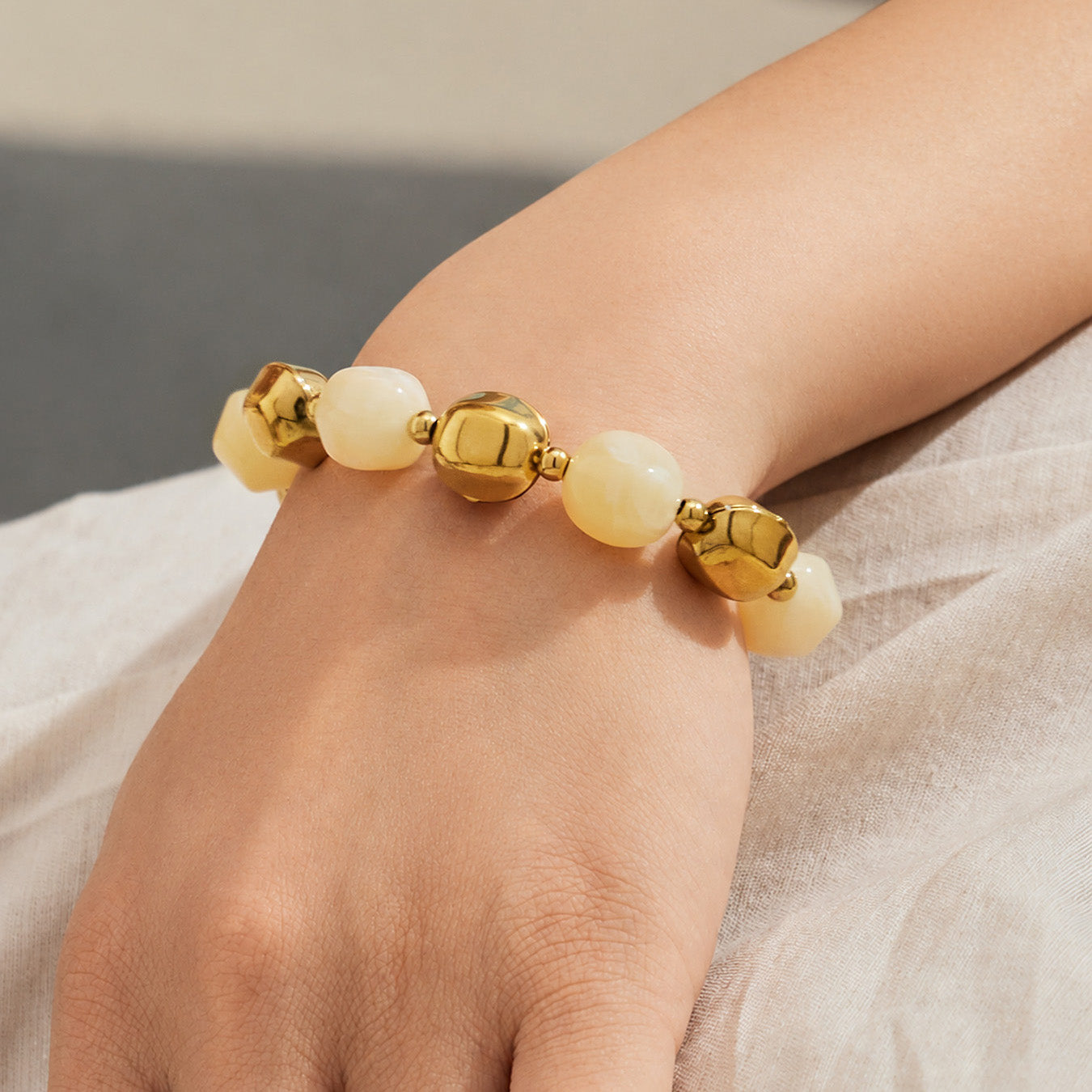Close-up of a cream resin bead bracelet with stainless steel accent beads worn on the wrist.
