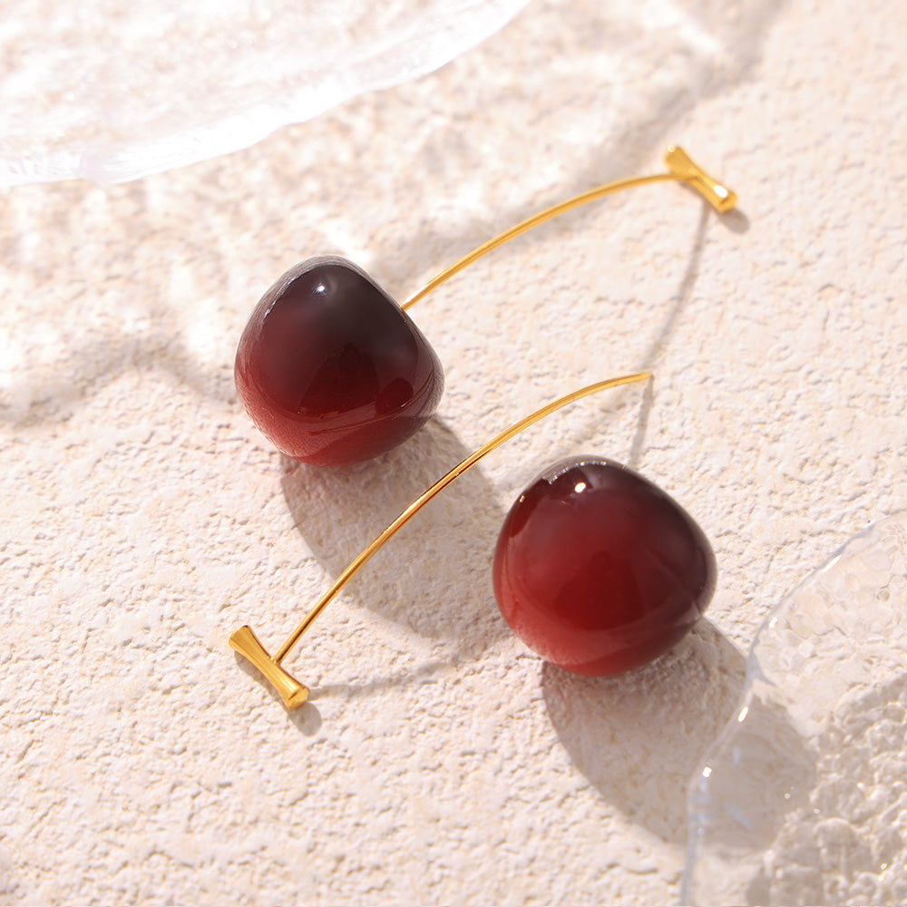 Deep red gradient cherry drop earrings arranged on a light textured background