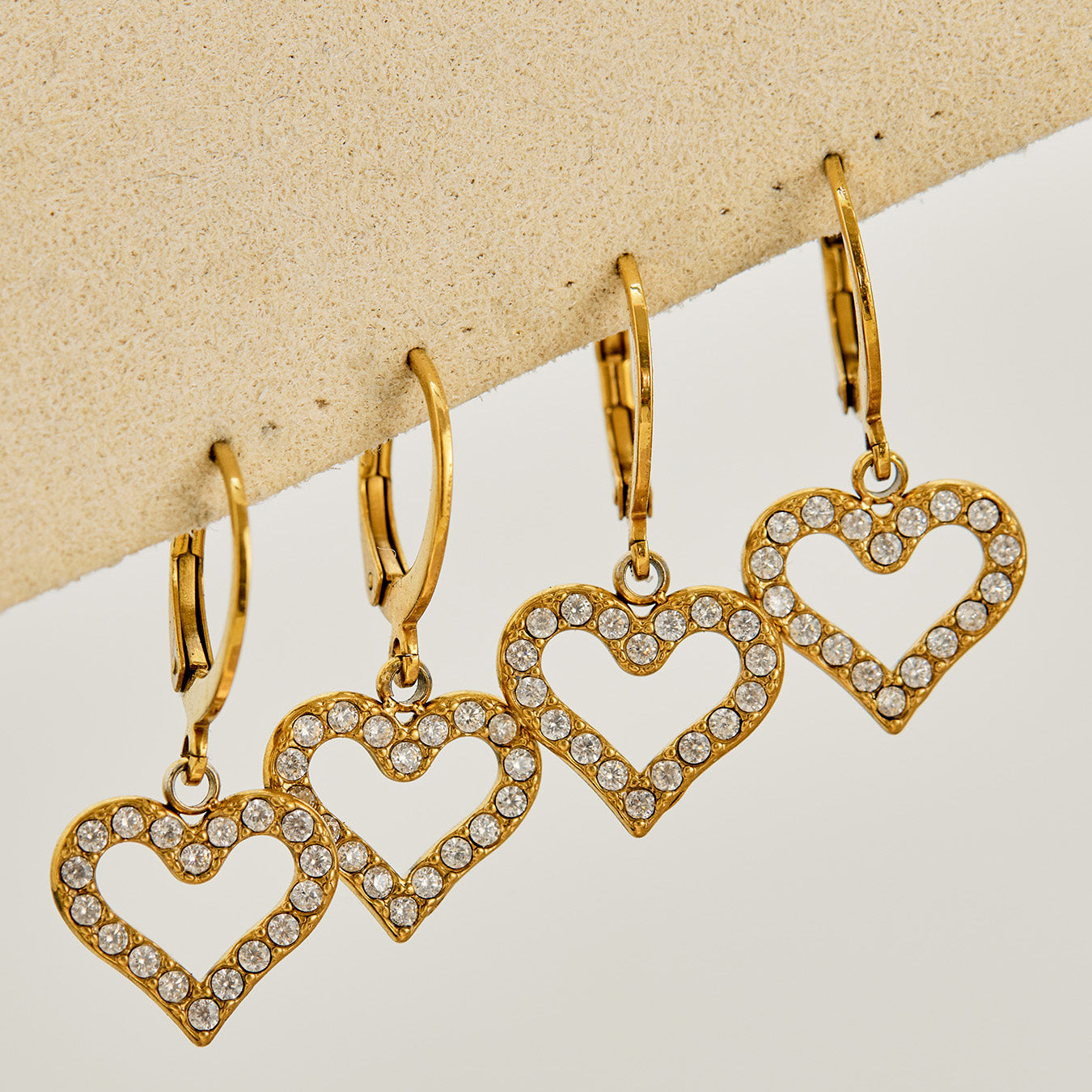 Multiple pairs of double heart drop earrings displayed in gold
