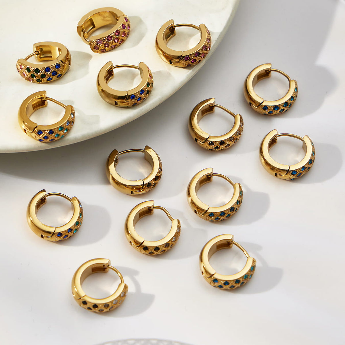 Gold-tone colorful CZ lattice hoop earrings arranged on a white surface with the hinged closures visible.