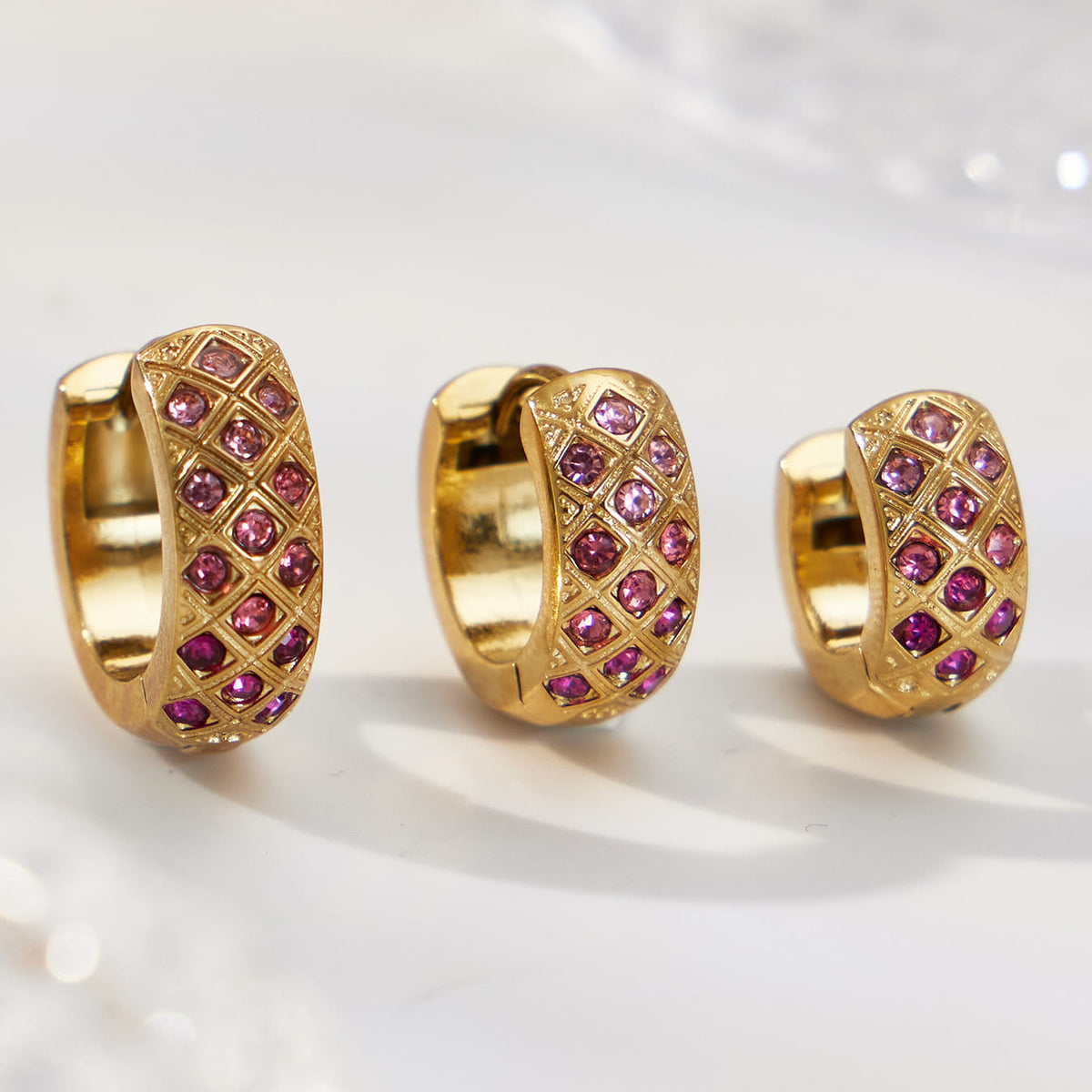 Three gold-tone pink CZ lattice hoop earrings in different sizes, shown from the side.