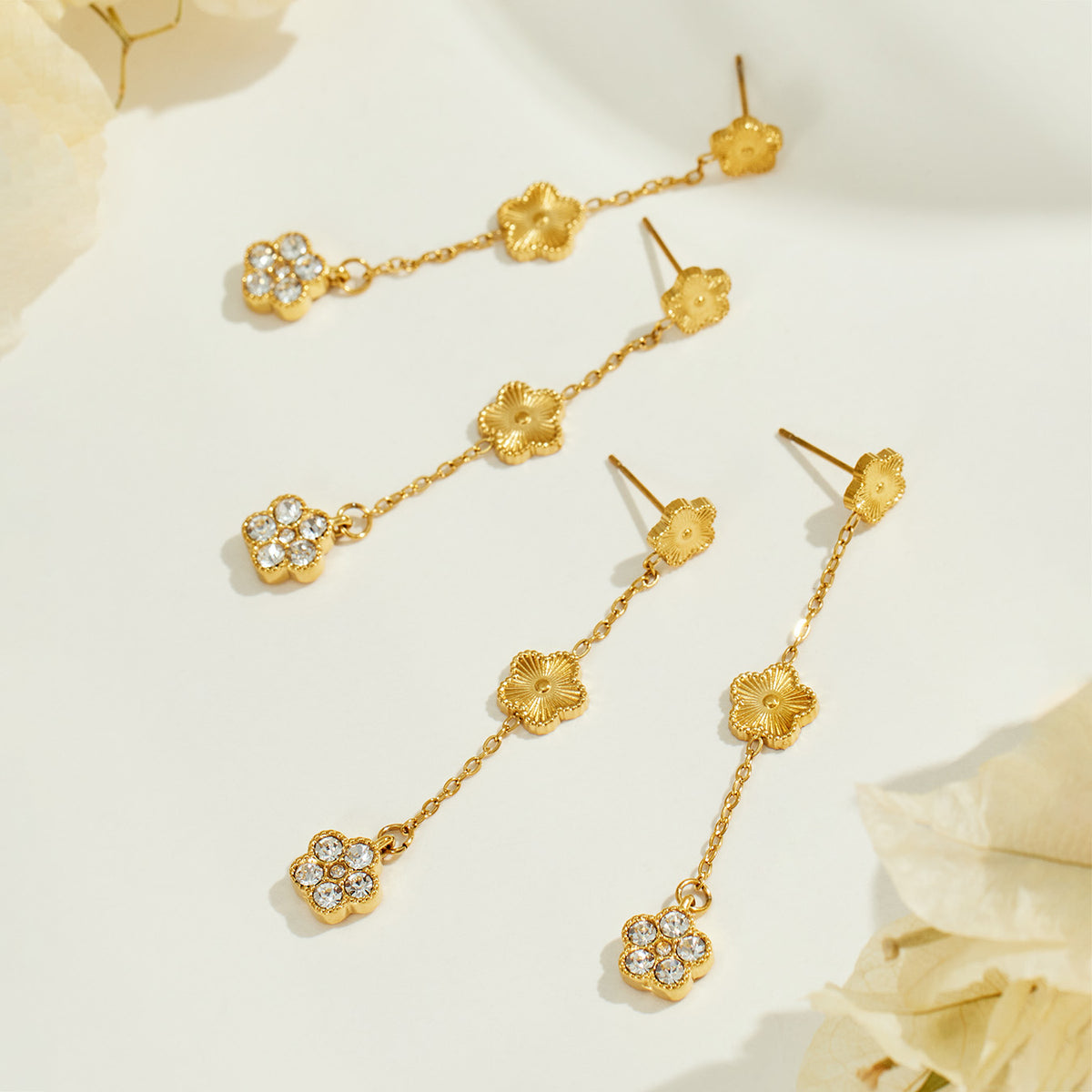 Gold floral dangle earrings arranged on a neutral surface with long chain drops and zircon flower charms