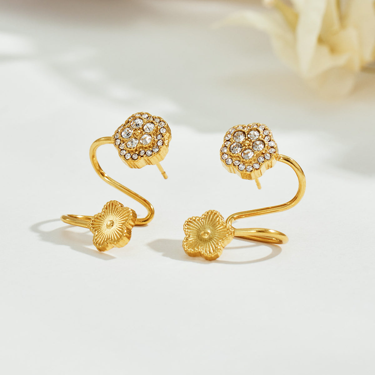 Gold floral ear cuff displayed on a neutral surface with zircon flower and sculptural spiral construction