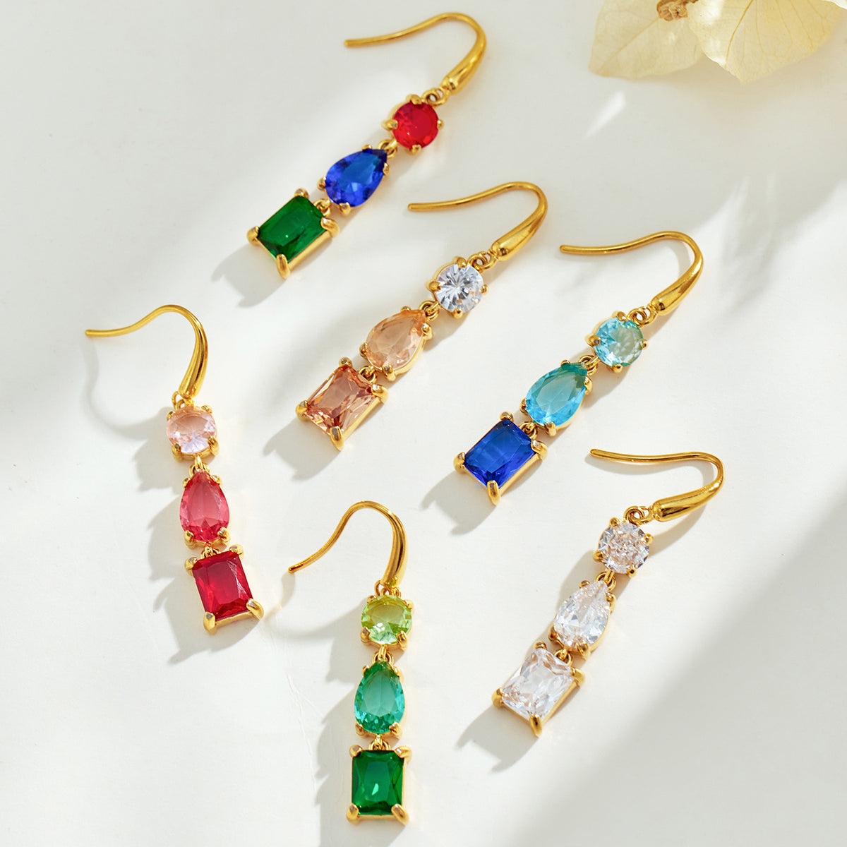 Flat lay of gold fishhook drop earrings in assorted red, blue, green, clear, champagne and multicolor stone combinations