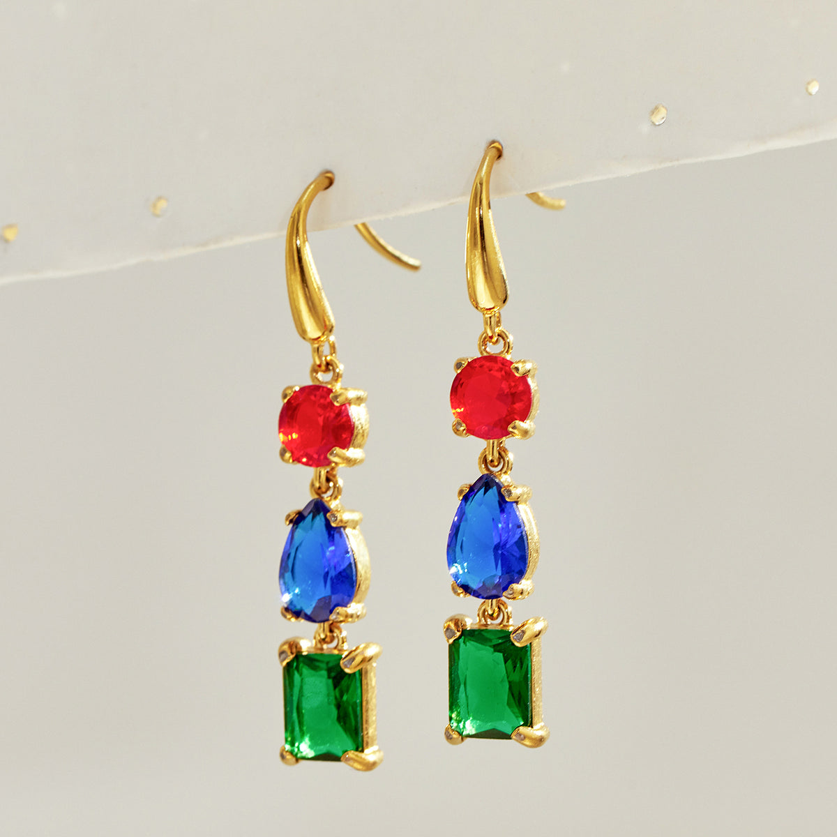 Pair of gold three-stone fishhook earrings featuring red round stones, blue pear-shaped stones and green rectangular drops