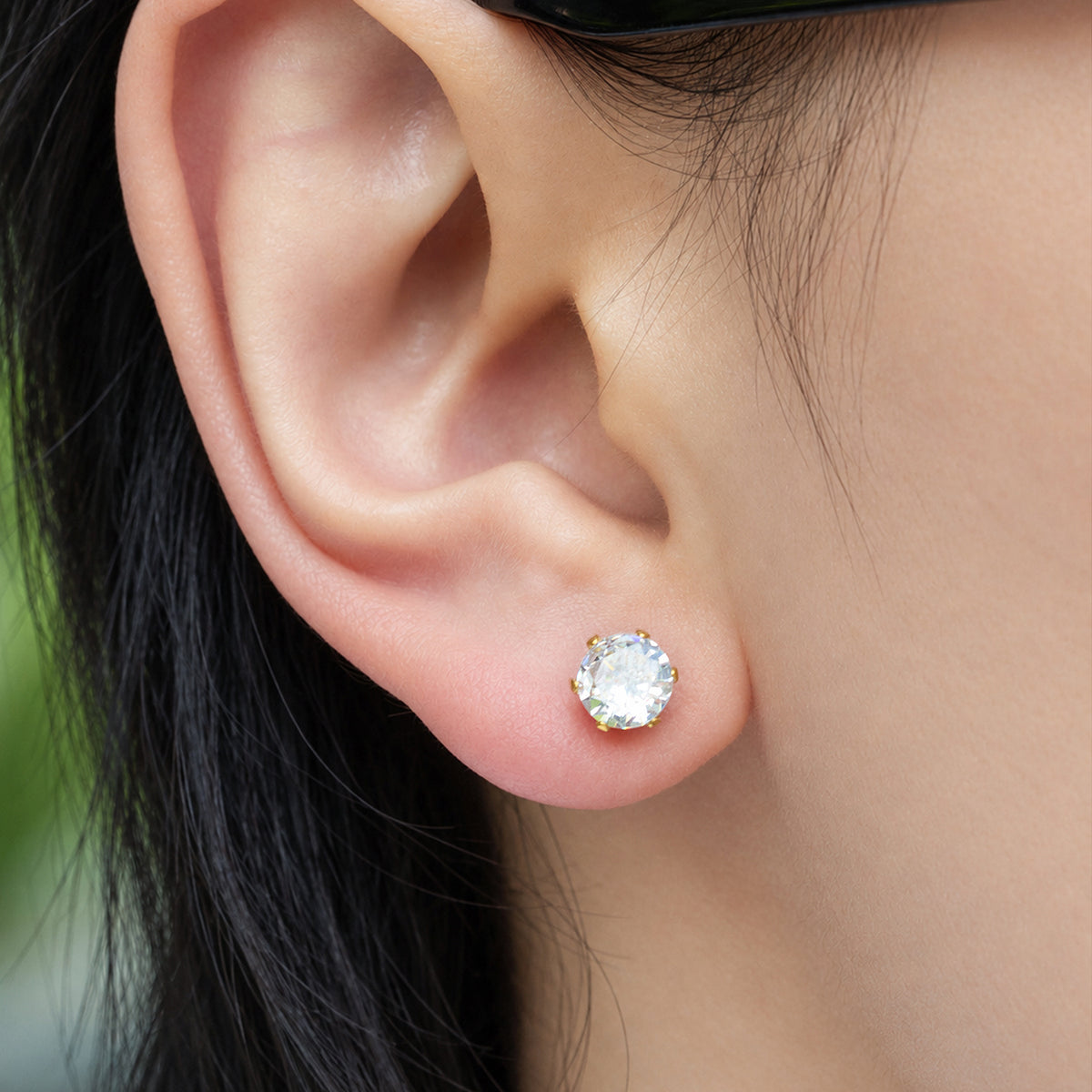 Close-up of a clear round stone stud earring set in polished gold-tone prongs on the earlobe