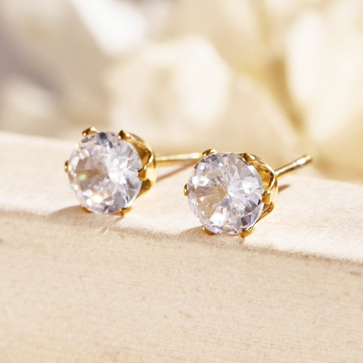 Close-up of gold six-prong solitaire stud earrings highlighting the faceted clear stones and polished settings