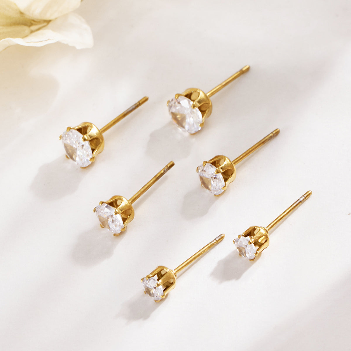 Gold-tone round stone stud earrings arranged on a light surface, showing their straight posts and prong settings