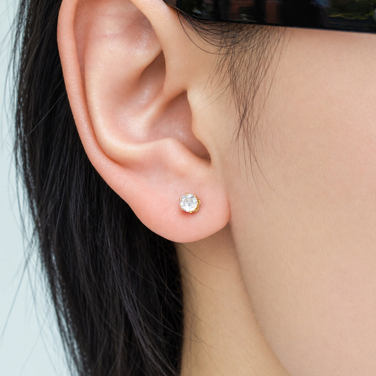 Small round clear stone stud earring worn on a model's earlobe for minimalist everyday styling
