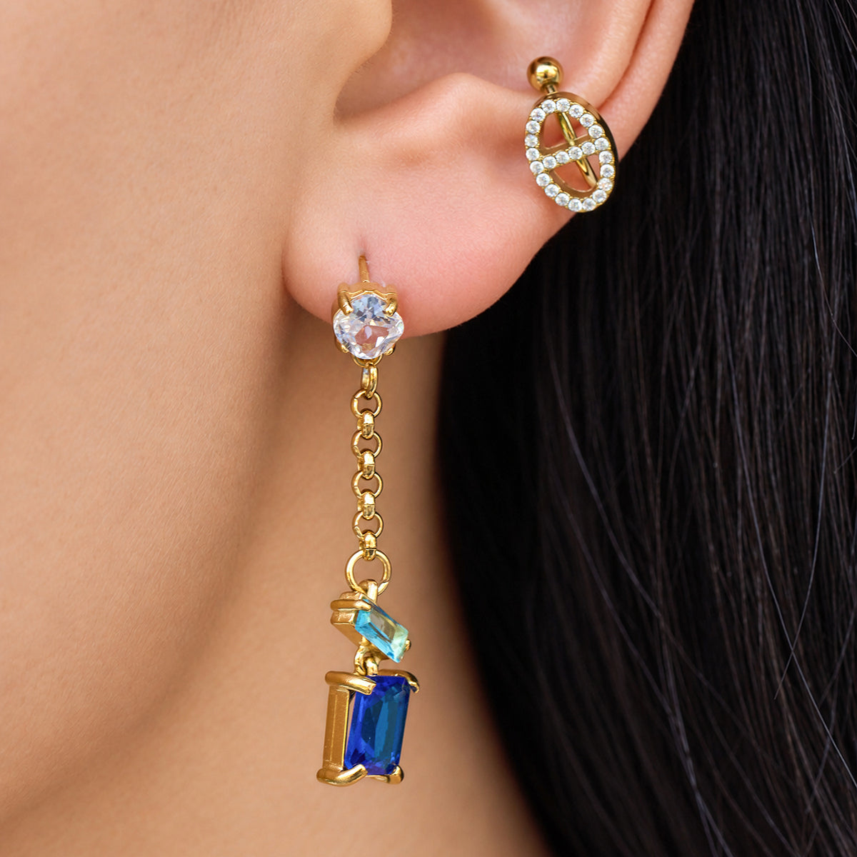 Close-up of blue zircon gold drop earrings worn on the ear with a long geometric dangle silhouette