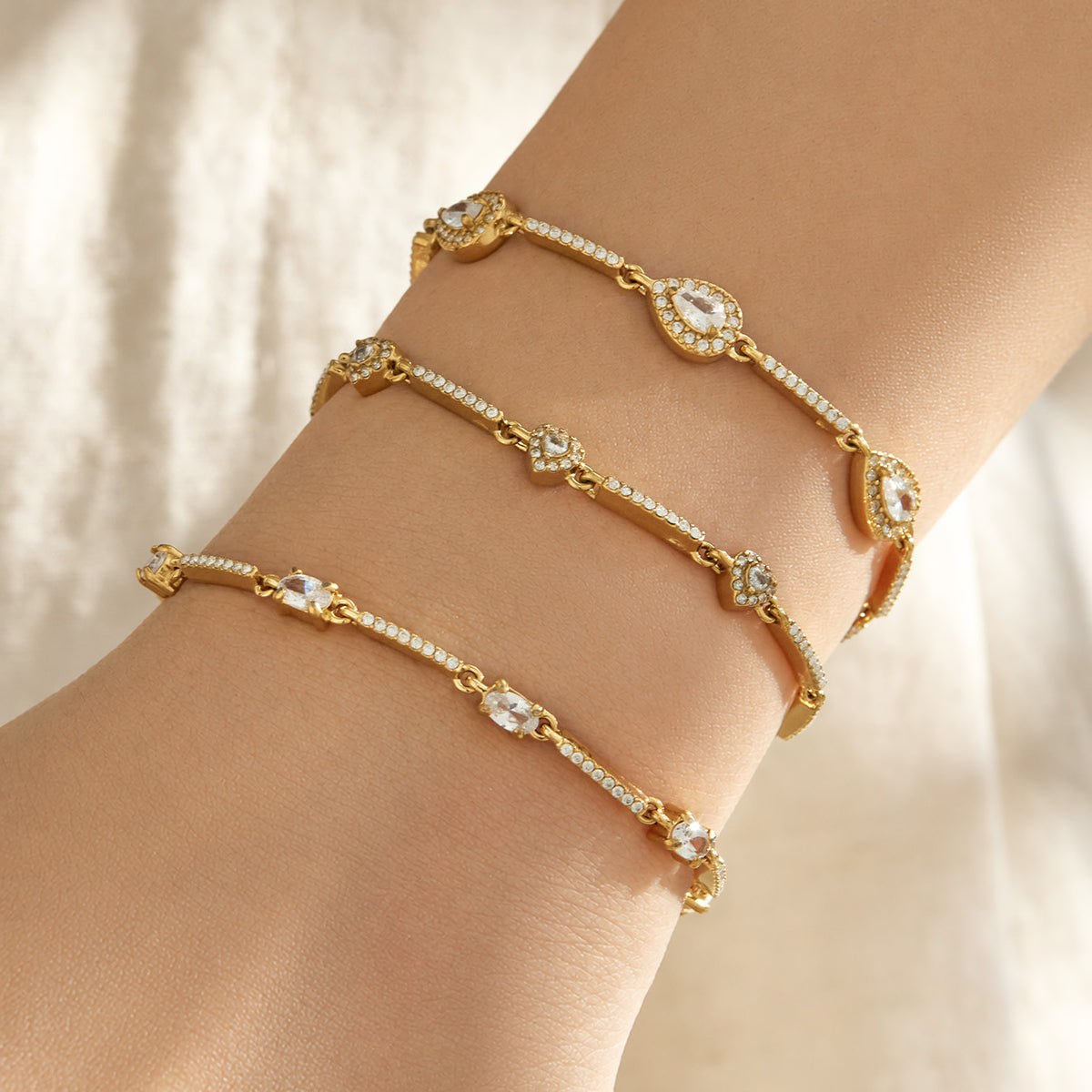 Close-up of gold zircon bracelets with different geometric motifs layered on a model wrist