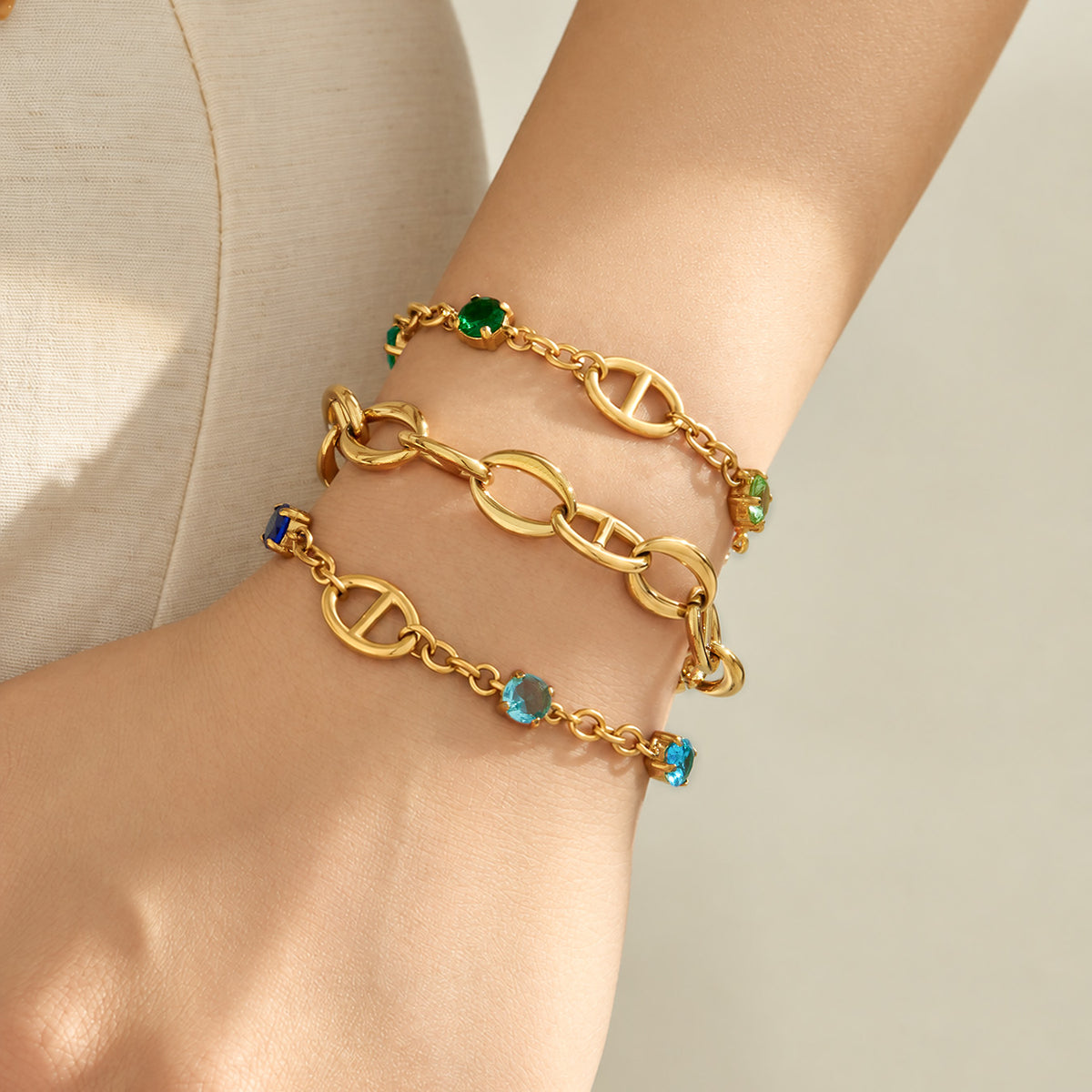 Three gold oval link bracelet styles worn together on a model wrist