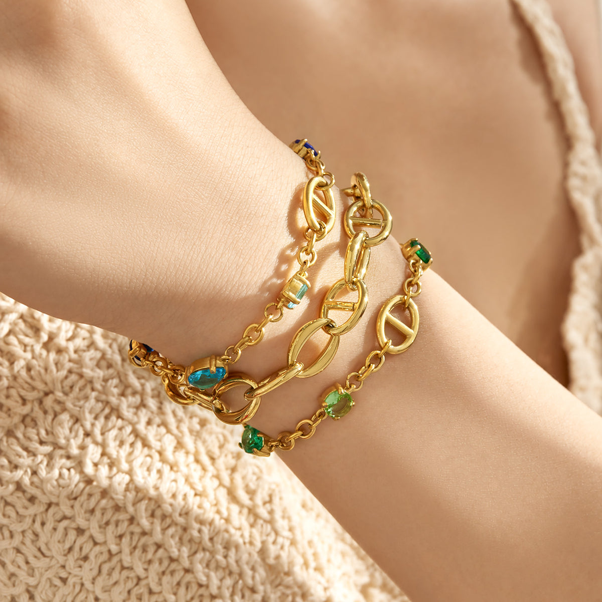 Close-up of gold oval link bracelets with green zircon and polished chain details