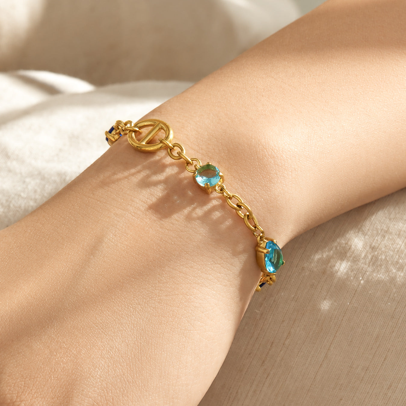 Gold oval link bracelet with blue and green zircon accents worn on the wrist