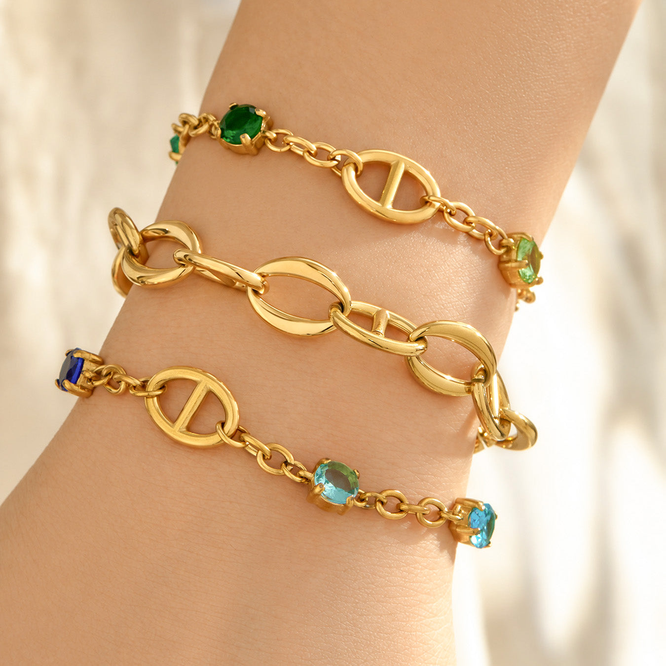 Gold oval link bracelets with green zircon accents layered on the wrist