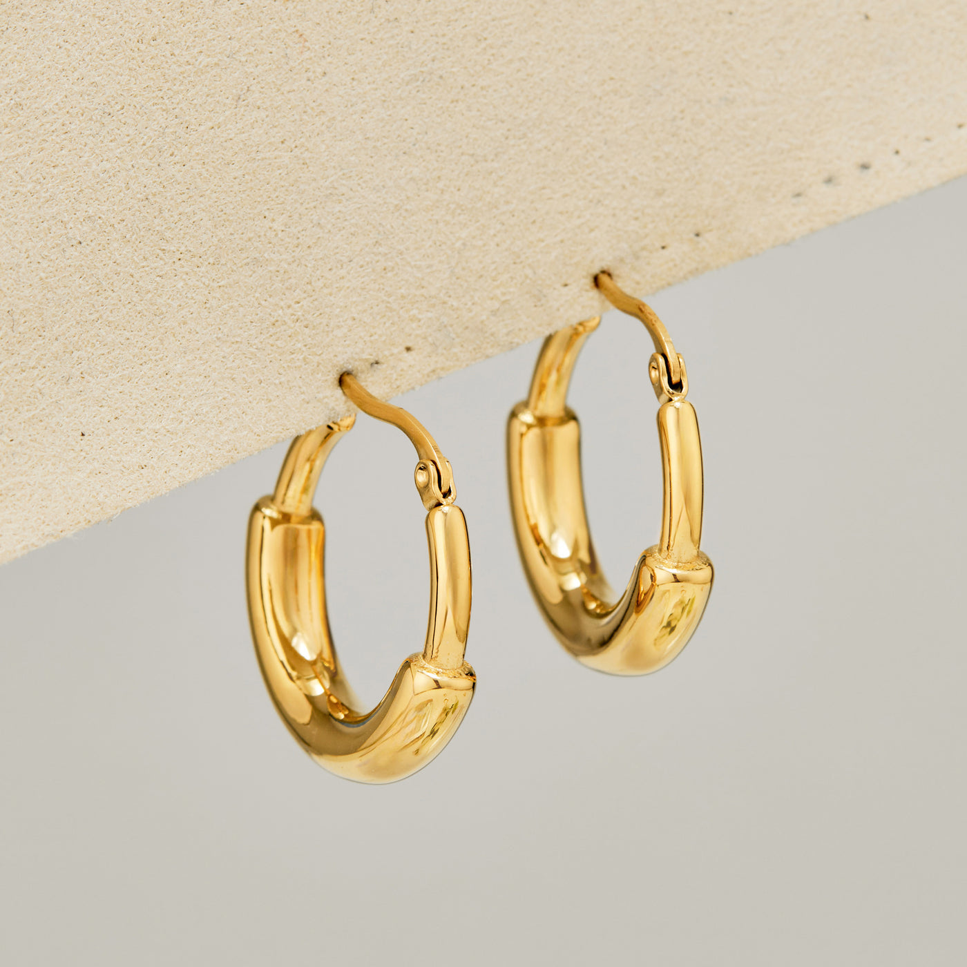 Gold C-shaped chunky hoop earrings displayed on a soft neutral surface