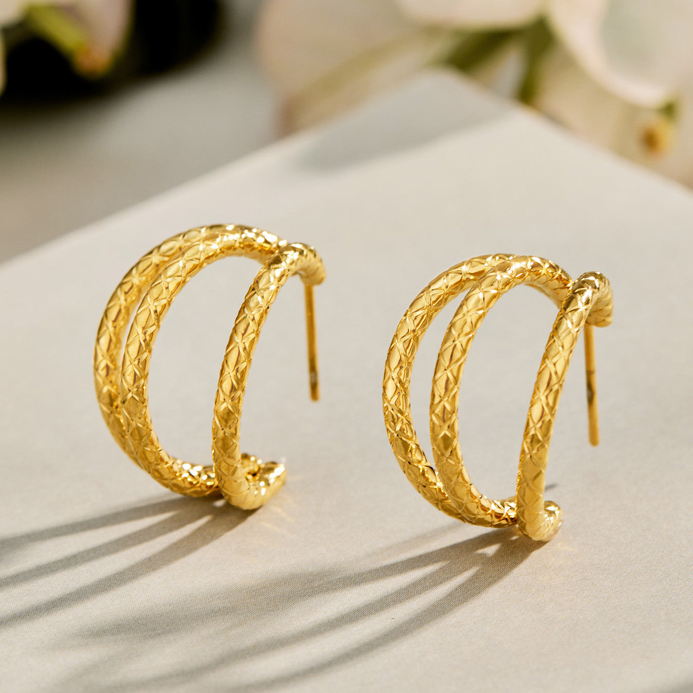 Pair of gold chunky double layer hoop earrings displayed on a reflective surface