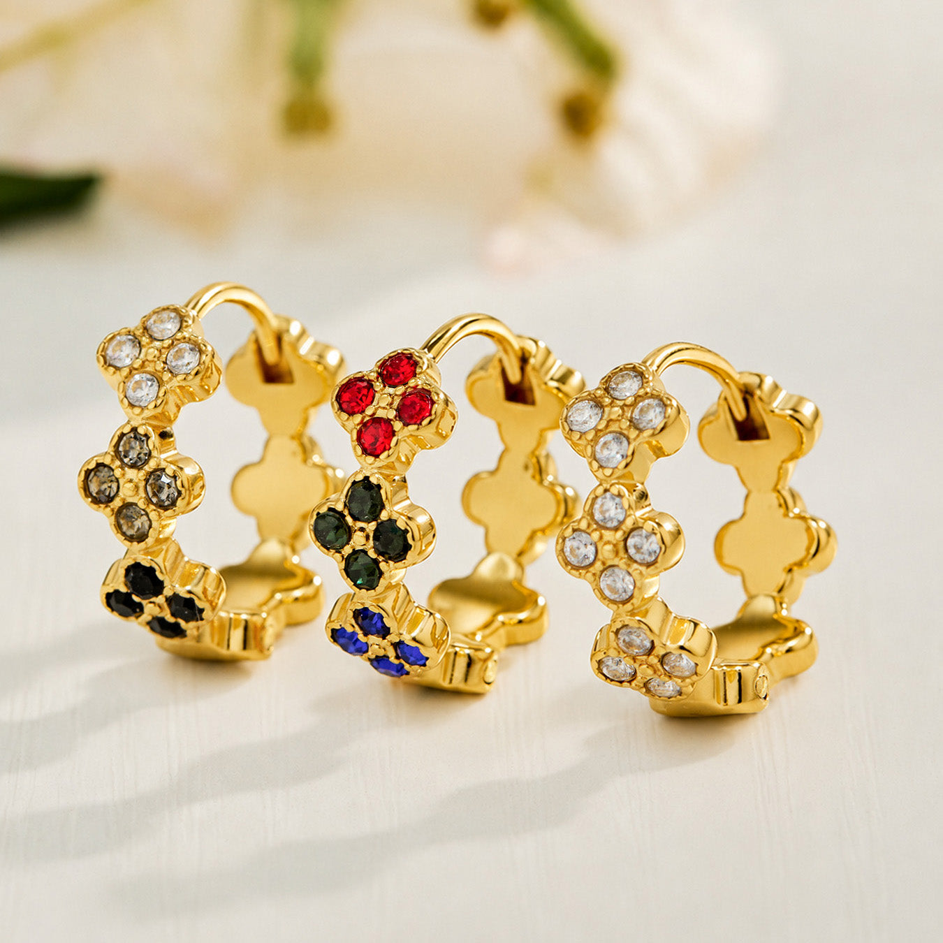 Gold four-leaf clover earrings displayed in white, multicolor and black CZ styles