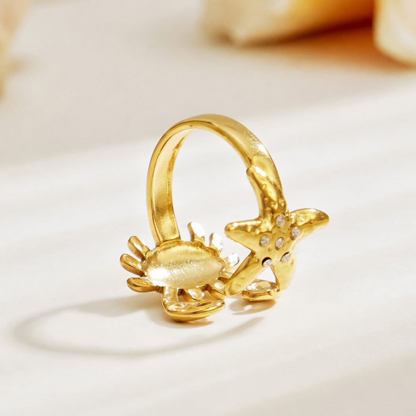 Side view of a gold crab and starfish open ring in 316L stainless steel with sculptural marine details