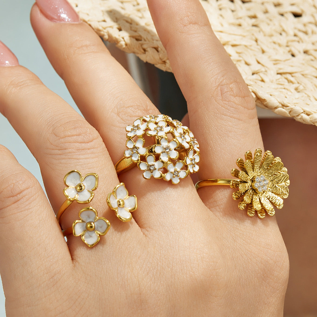 Close-up of gold daisy and enamel flower rings styled together on a model hand